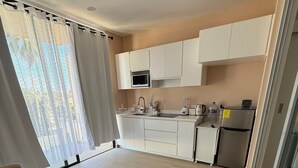 Apartamento moderno com cozinha compacta, sofá e uma grande janela com cortinas.