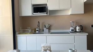 Uma cozinha moderna com armários brancos, micro-ondas, pia e bancada com liquidificador e utensílios.