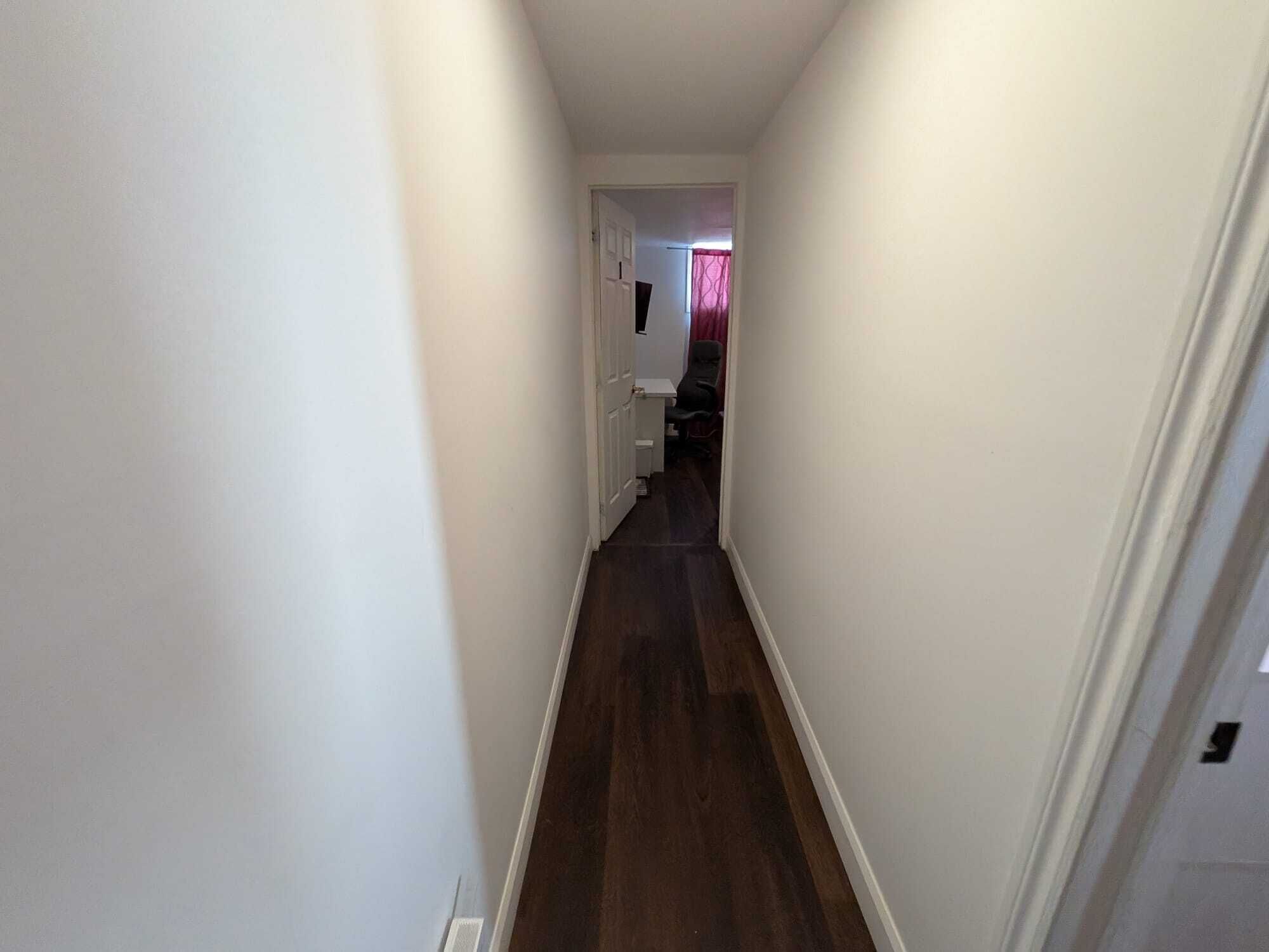 A narrow hallway with white walls and dark wooden flooring.