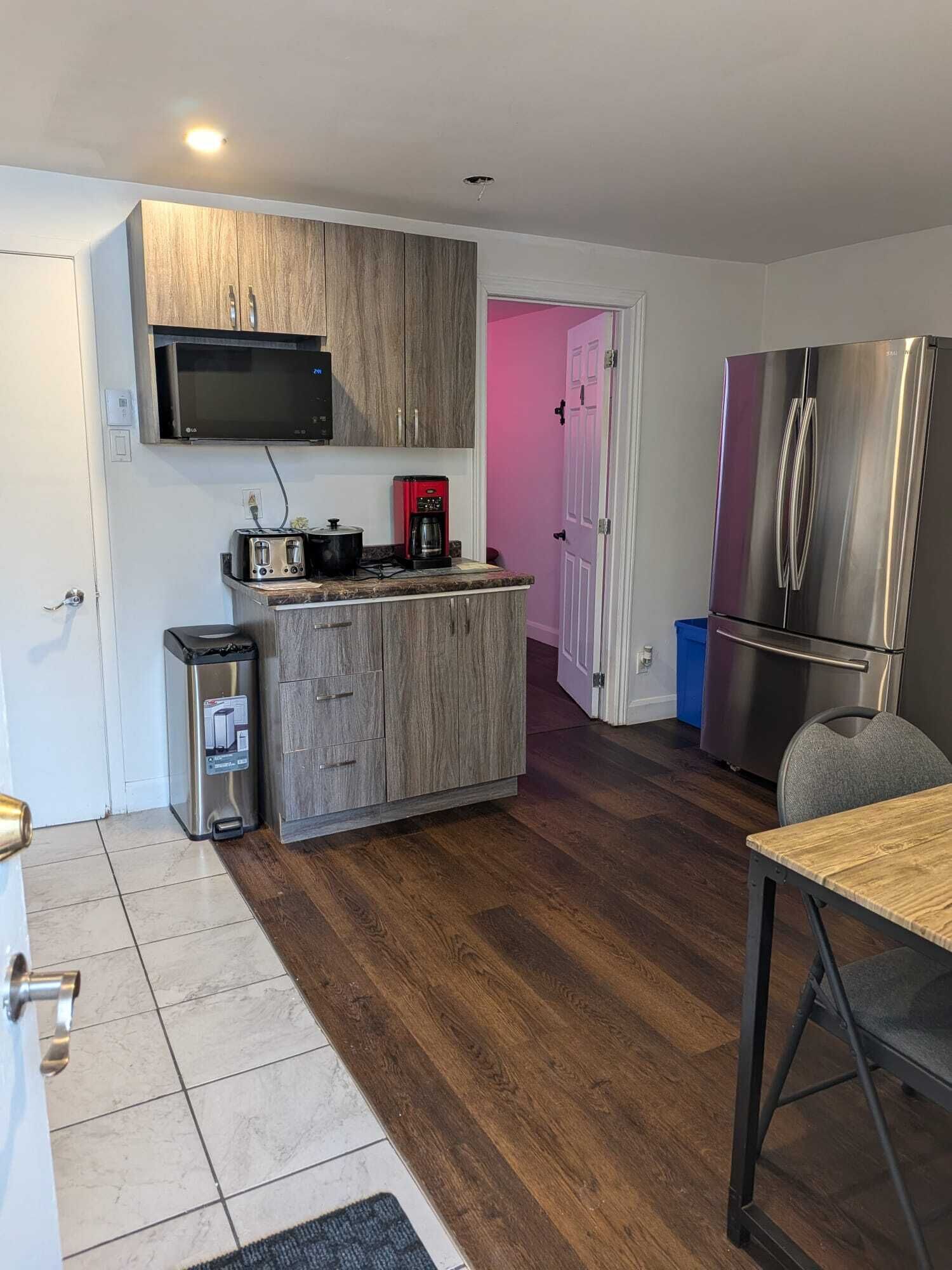 A compact kitchen with wooden cabinets, a microwave, a coffee maker, and a stainless steel refrigerator.