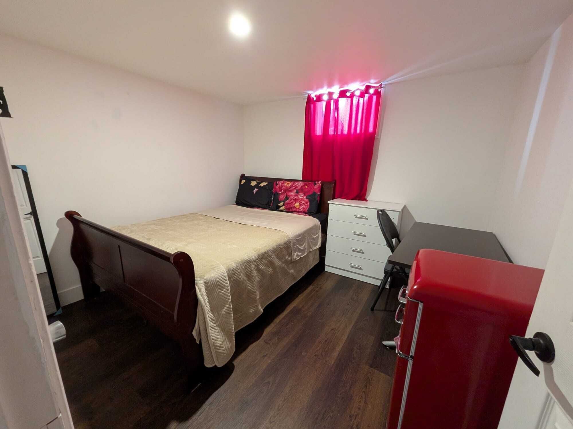 A small, neatly arranged bedroom with a bed, a desk, and a dresser.