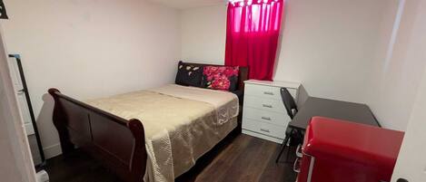 A small, neatly arranged bedroom with a bed, a desk, and a dresser.
