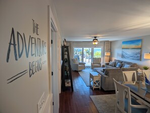 A living room with a sofa, chairs, a coffee table, and a bookshelf. There is a large window with a view of the outdoors. - Sunset Balcony + 2 King Suites + Beach Gear (Fort Walton Beach)