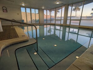 Una piscina interior con paredes de vidrio transparente, suelo de baldosas y baranda de metal.