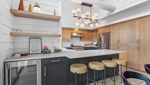 A modern kitchen with wooden cabinets, a stainless steel refrigerator, and a bar area with stools. - Steps to Slopes  Hot Tub -  Modern Mtn Retreat (Sandpoint)