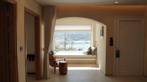 A room with a view of a coastal city, a bench, and a door. - | Utopia Luxury Suite | (Pigadia)