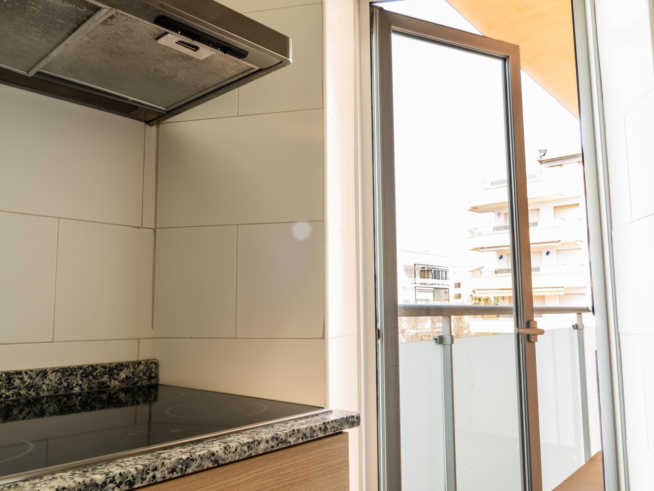 A kitchen with a granite countertop, a stainless steel range hood, and a sliding glass door leading to a balcony.