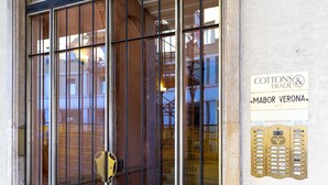 Een gevel met een metalen poort, een mozaïek vloer en een bordje voor 'Cottons & Trade' met 'Mabor Verona' eronder.