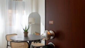 Een houten deur met een naambordje met de naam 'Aida', een ronde tafel met stoelen en een kamerplant in een eetruimte.