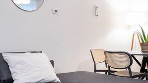 Una habitación moderna con un sofá gris, un espejo redondo, una mesita con sillas y una planta en maceta.