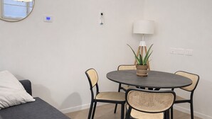 Una sala moderna con un sofá gris, una mesa redonda de comedor con sillas de mimbre, una planta en maceta y una lámpara colgante.
