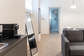 Una cocina moderna con cafetera, un espejo grande y un sofá gris en una habitación luminosa con suelo de madera.