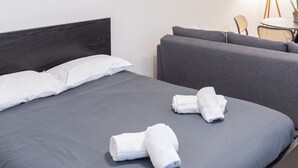 Una habitación de hotel moderna con cama, sofá gris y un espejo redondo en la pared.
