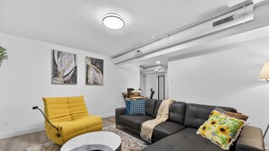 A modern living room with a yellow armchair, a black sofa, and a coffee table. - 2BR | Warm | King Bed | Downtown | Expo Centre | Roger's Place (Edmonton)
