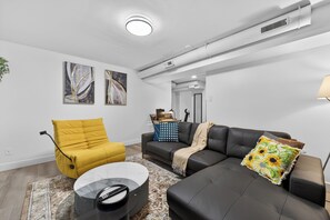 Ett modernt vardagsrum med en gul fåtölj, en svart soffa och ett soffbord.