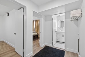 Moderni hotellihuone, jossa on puulattia, musta matto, beigenvärisillä verhoilla varustettu sänky, peilillä varustettu kylpyhuone ja pyyhekoukku.