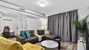 A modern living room with a sectional sofa, a yellow armchair, a round coffee table, and a TV on a white stand. - 2BR | Warm | King Bed | Downtown | Expo Centre | Roger's Place (Edmonton)