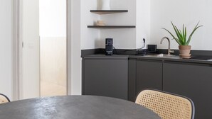 Eine moderne Küche mit dunkler Arbeitsplatte, einem Regal mit einer Vase, einer Topfpflanze und einer Kaffeemaschine.