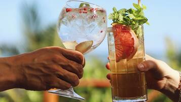 Two people holding drinks, one with a clear glass and one with a tall glass, outdoors with a blurred background.