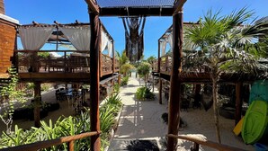 A wooden deck with a net canopy, surrounded by tropical plants and a sandy path. - Casa Hayhu Beach (Mahahual)