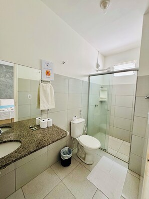 Un baño moderno con encimera de granito, inodoro, cabina de ducha de vidrio y un espejo grande.