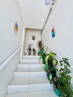 Una escalera con peldaños blancos, plantas en macetas a los lados y elementos decorativos colgando en las paredes.