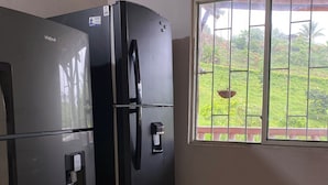 A kitchen with a black refrigerator and a window with a view of greenery.