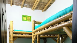 A room with two bunk beds made of bamboo, a green wall decoration, and a tiled floor.