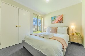 A bedroom with a bed, a nightstand, a lamp, a painting, and a sliding door. - StayAU 4BR Family Retreat with Garden (Seville Grove)
