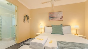 A hotel room with a bed, two bedside lamps, a painting on the wall, and a shower area. - StayAU 4BR Family Retreat with Garden (Seville Grove)