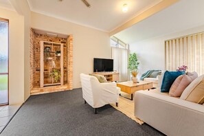 A modern living room with a sofa, a coffee table, a TV, and a brick accent wall. - StayAU 4BR Family Retreat with Garden (Seville Grove)