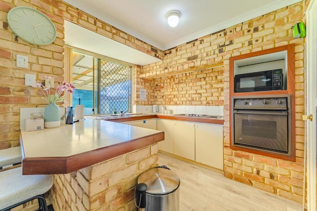 Una cucina con pareti in mattoni, un piano di lavoro in legno, forno a incasso e un orologio appeso al muro.