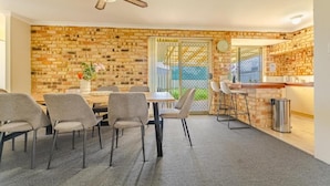 A dining area with a brick wall, a ceiling fan, a table with chairs, and a kitchen counter. - StayAU 4BR Family Retreat with Garden (Seville Grove)