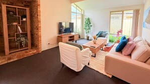 A living room with a brick accent wall, a television, a sofa, and a coffee table. - StayAU 4BR Family Retreat with Garden (Seville Grove)