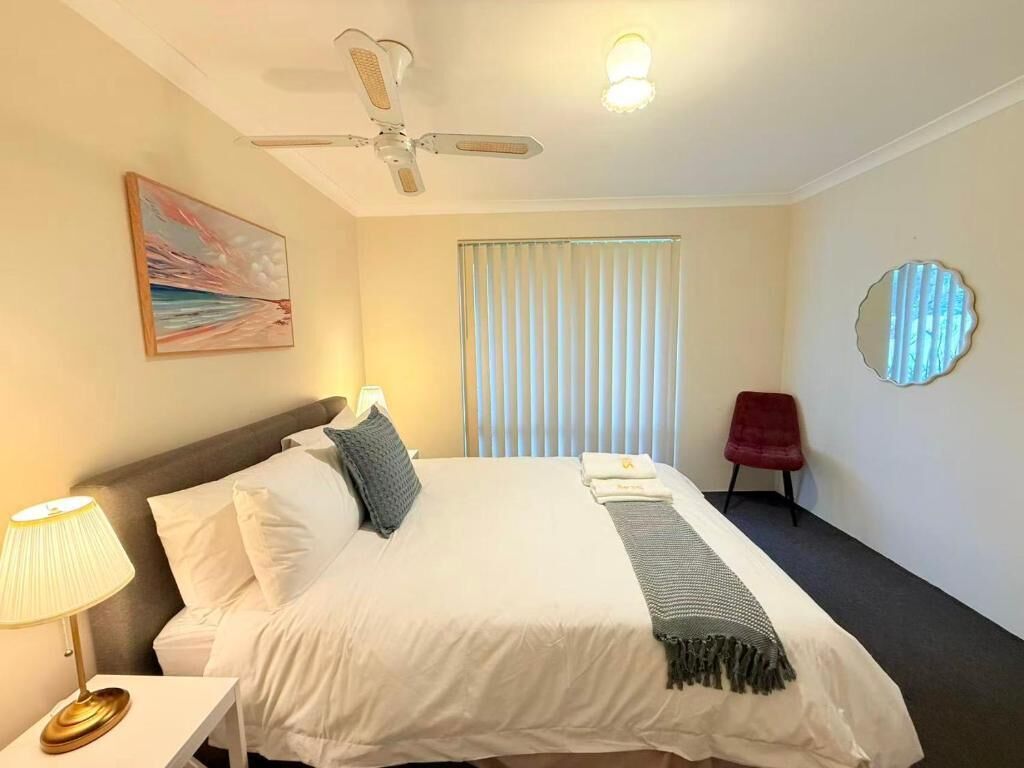 Una habitación de hotel con una cama, un ventilador de techo, una ventana con persianas, una silla roja y un espejo montado en la pared.