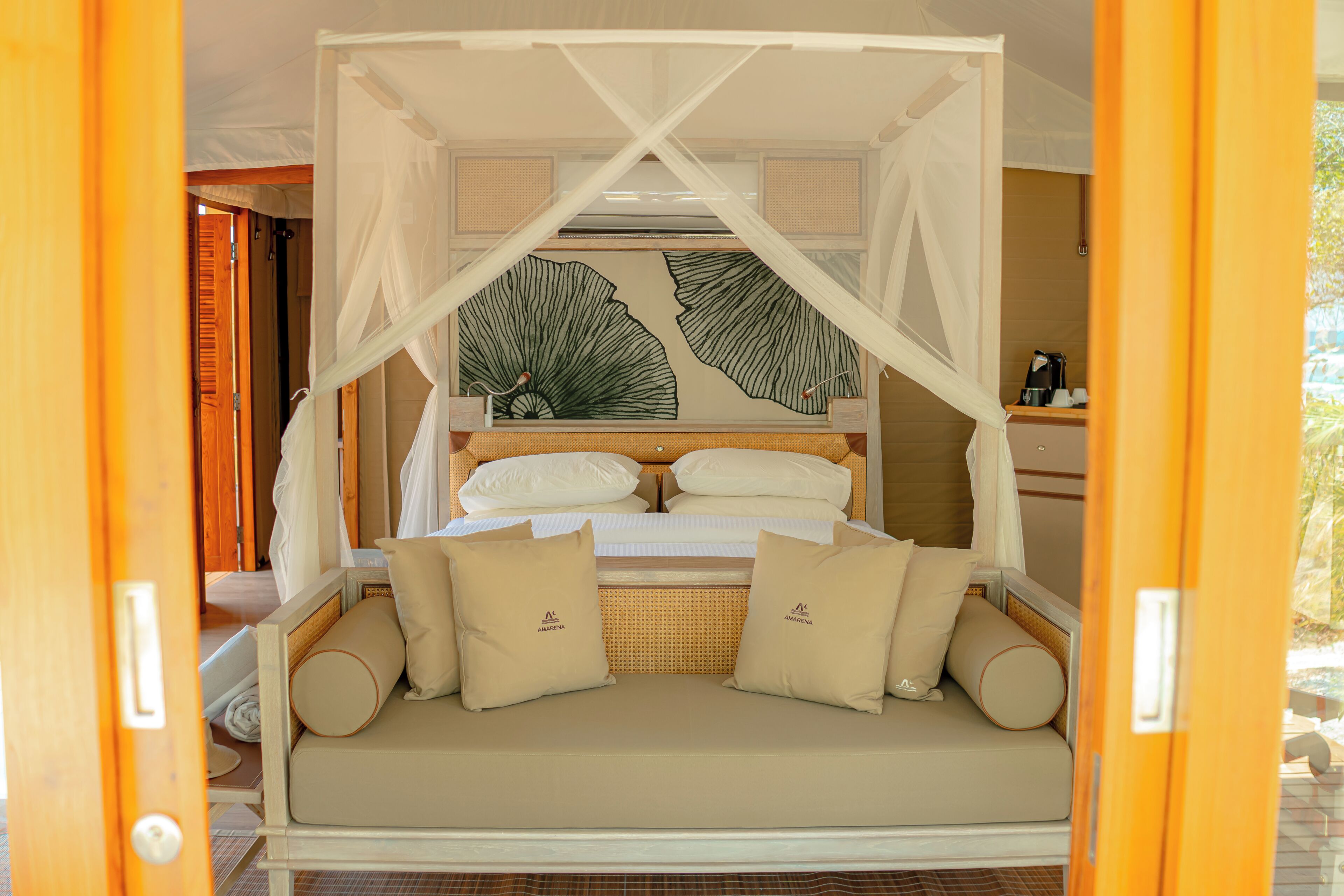 A bed with a canopy, a sofa with cushions, and a wall with a leaf pattern.