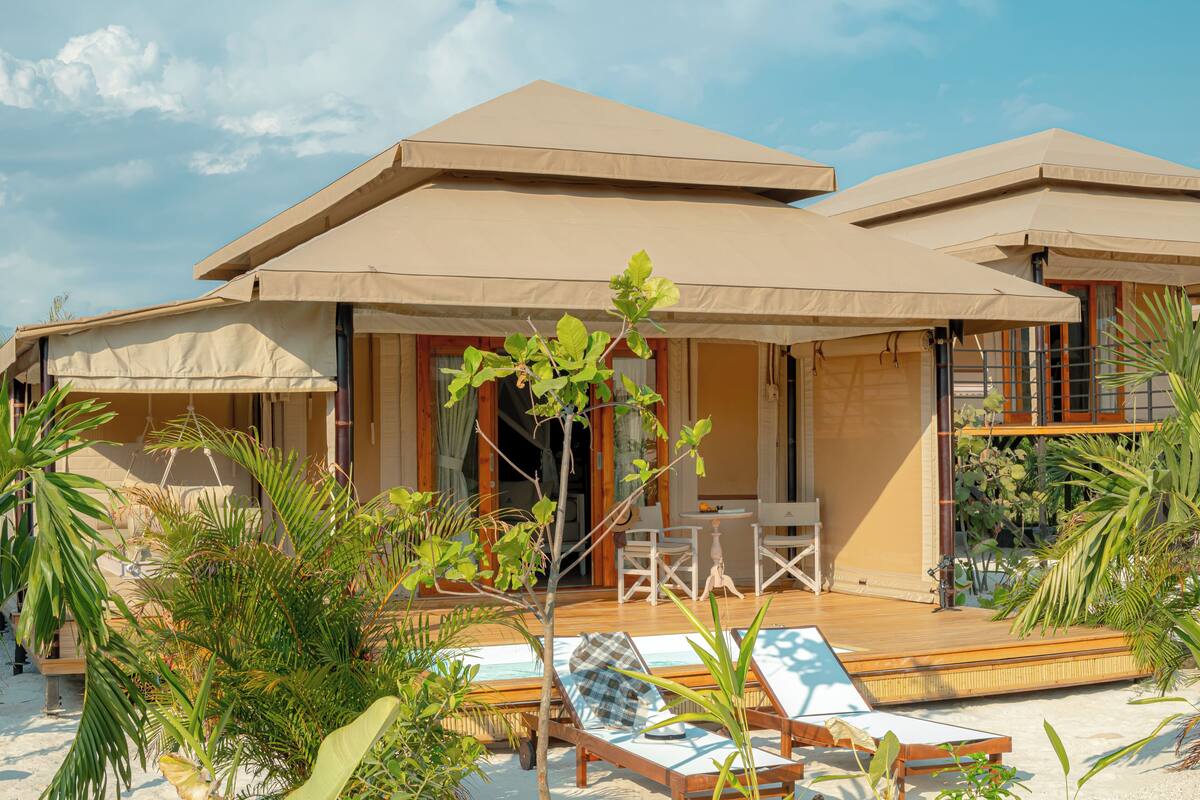 A resort with outdoor seating, a pool, and tropical plants.