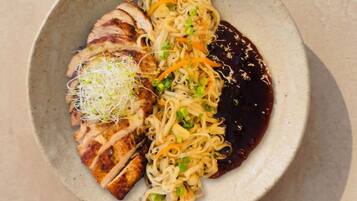 A plate of food with noodles, sliced meat, and a dark sauce.