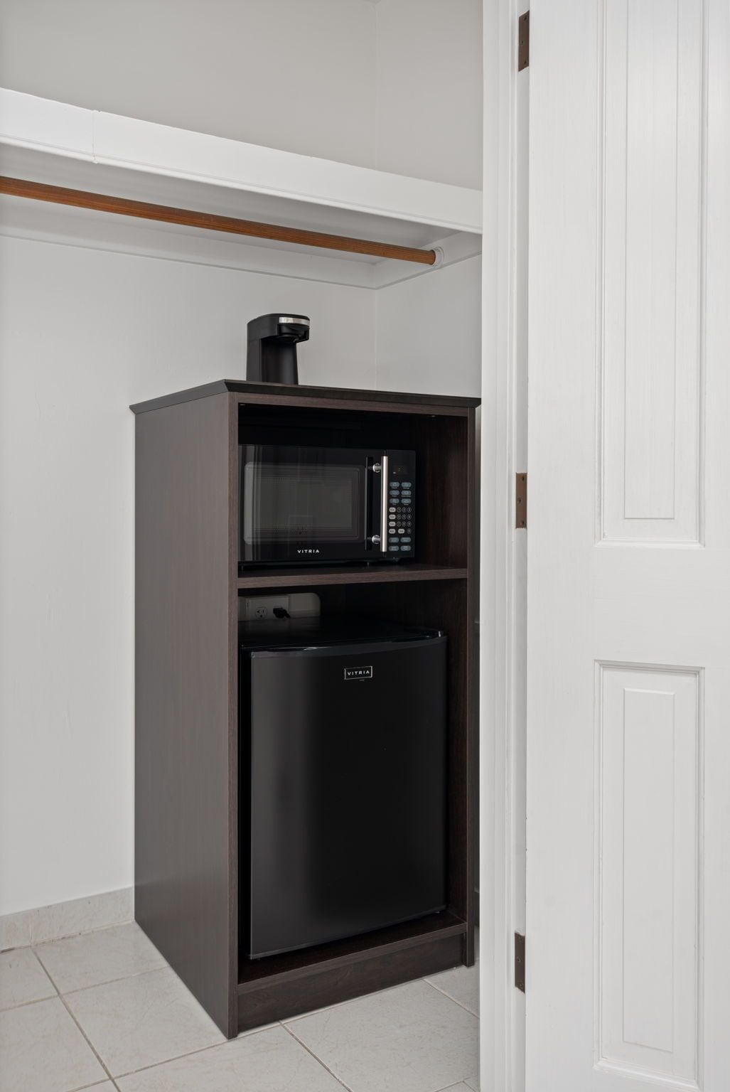 A compact kitchenette with a microwave and refrigerator, built into a dark cabinet against a white wall.