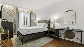 A bedroom with a bed, bedside tables, a desk, a chair, a TV, and a stone accent wall.