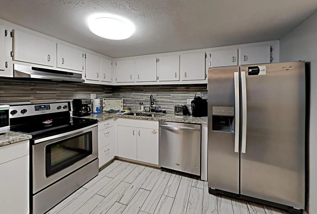 A modern kitchen with stainless steel appliances, white cabinets, and a tiled backsplash.