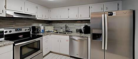 Una cocina moderna con electrodomésticos de acero inoxidable, armarios blancos y salpicadero de azulejos.