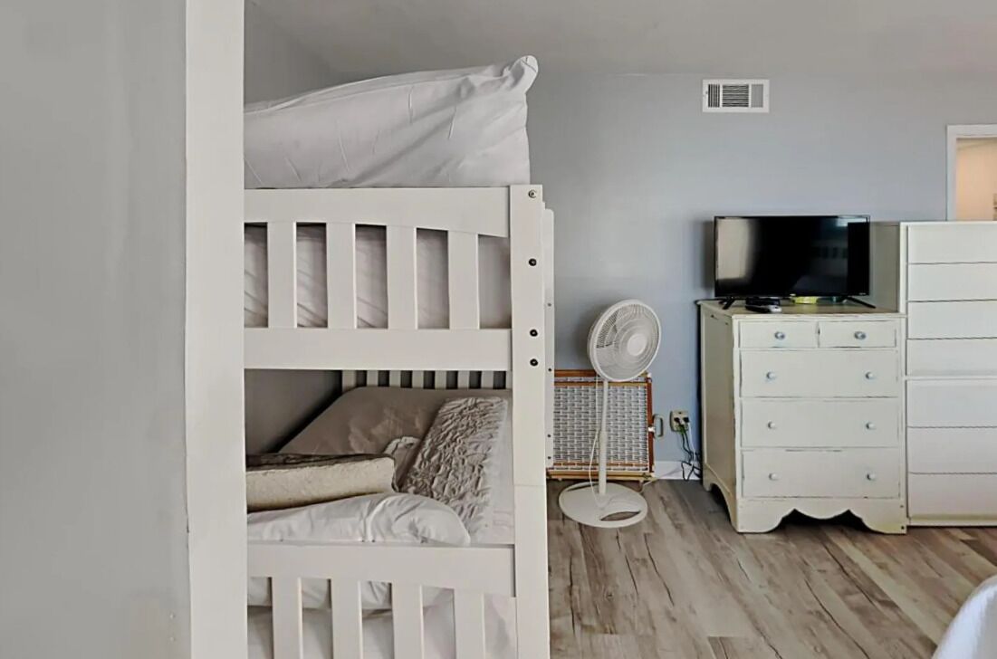 A room with a bunk bed, a white dresser, a television, and a fan.