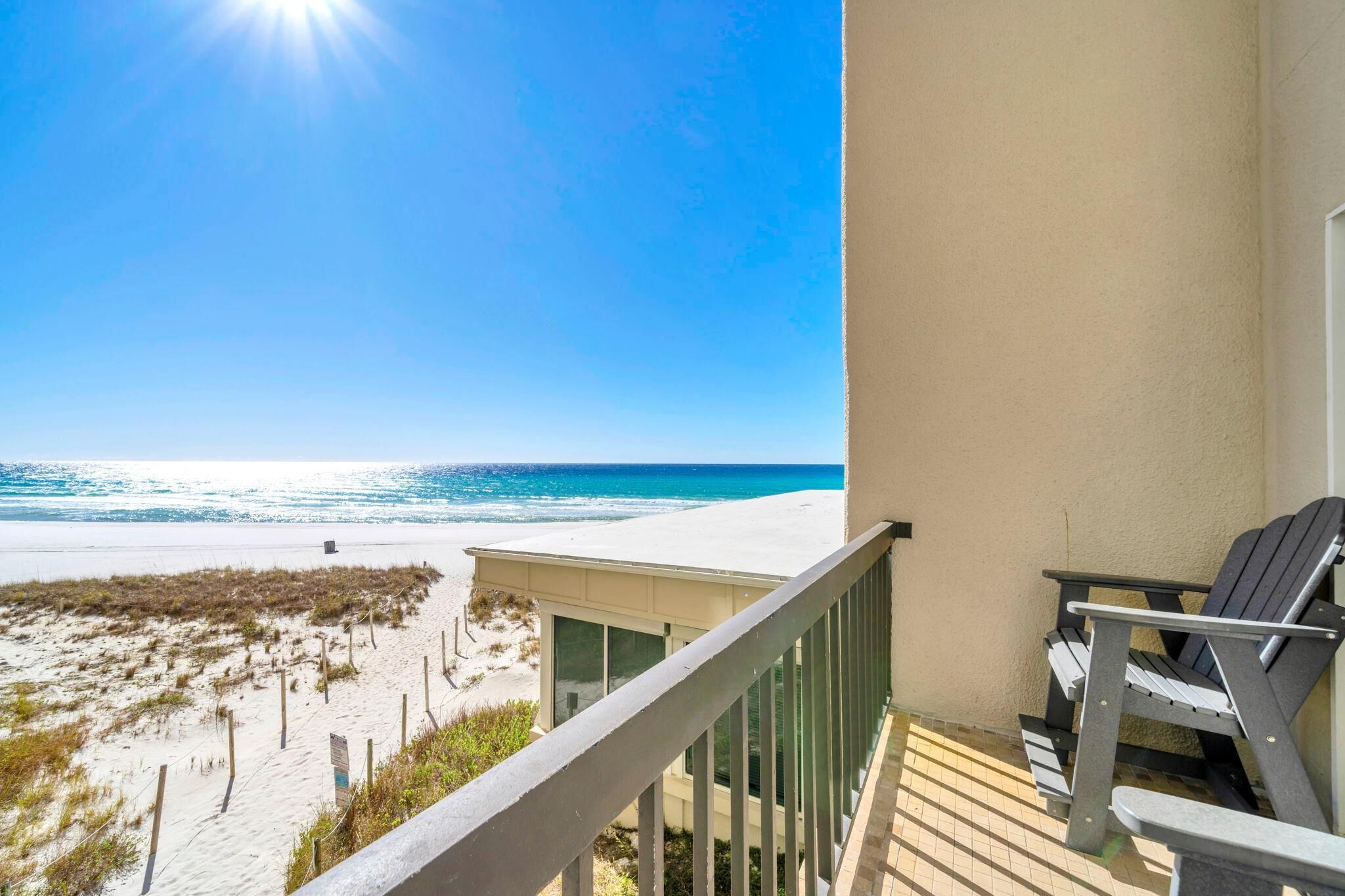 A balcony with a view of the beach, a chair, and a small building.
