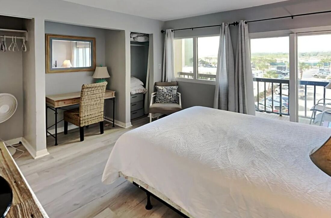 A hotel room with a bed, a desk, a chair, a wardrobe, and a balcony with a view.
