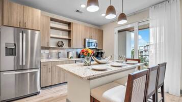A modern kitchen with a central island, stainless steel appliances, wooden cabinets, and pendant lighting.