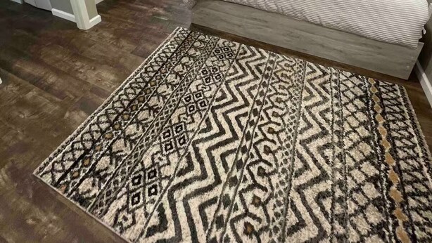 A bedroom with a bed, a dresser, a television, and a patterned rug.
