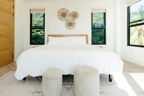 A bedroom with a large bed, two windows, a wooden door, and wall decor. - Luxury Home | Harbor Views | Central St George`s (Saint George's)