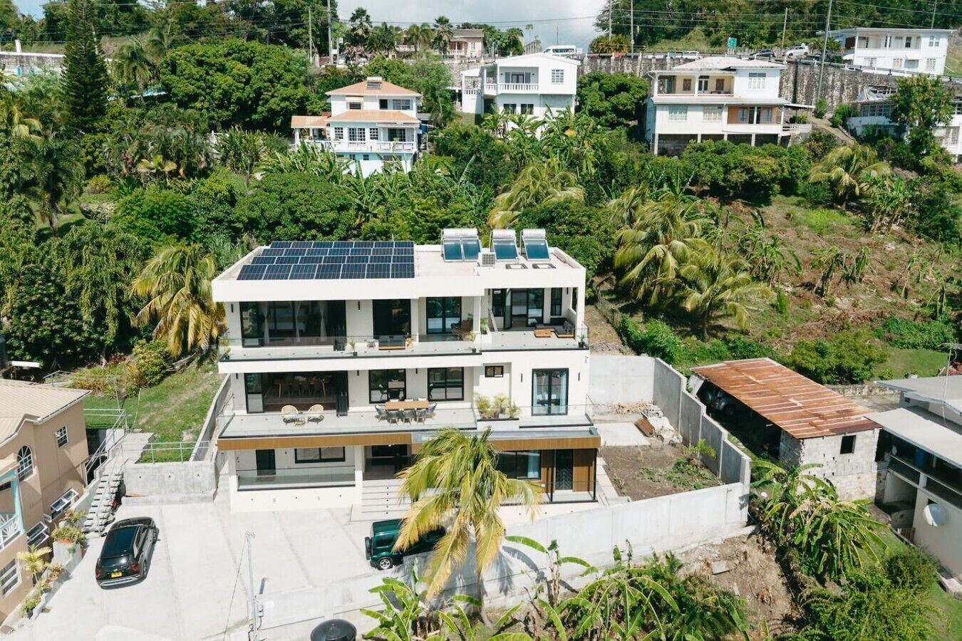Un edificio residencial de varios pisos con paneles solares en el techo, rodeado de exuberante vegetación y otras viviendas.