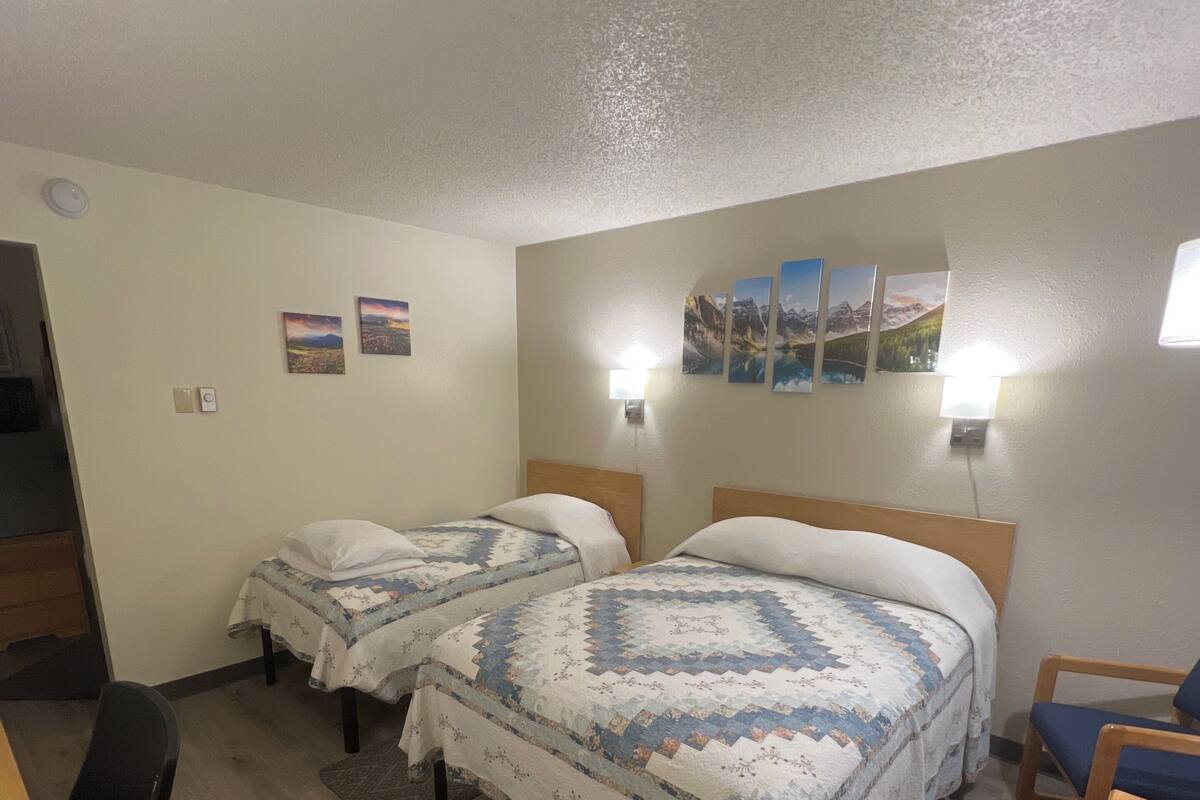 A hotel room with two beds, a desk, a chair, and a rug.